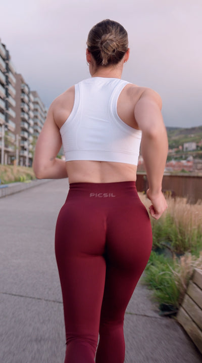 Mujer de espaldas corriendo con unas mallas granate y un top blanco